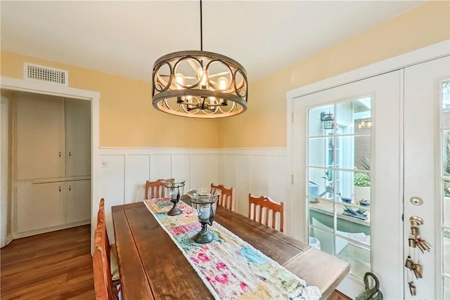 dining area with wood finished floors, a chandelier, a wainscoted wall, and a decorative wall
