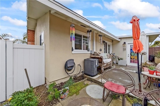view of front of house with stucco siding, fence, central AC unit, and a patio