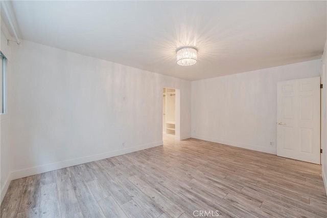 unfurnished room with light wood-style floors, baseboards, and a chandelier