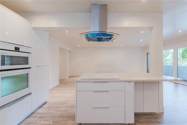 8963 Burton Way Unit 103, Los Angeles, CA 90048 - kitchen with modern cabinets, island exhaust hood, white cabinetry, light wood finished floors, and recessed lighting