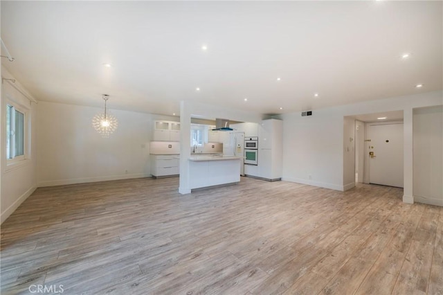 unfurnished living room featuring light wood-style flooring, a chandelier, baseboards, and recessed lighting