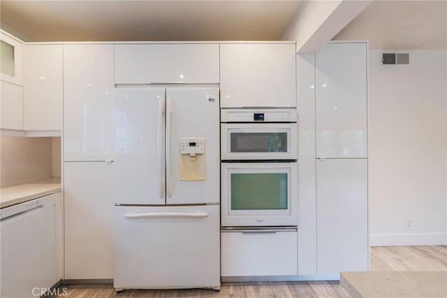kitchen featuring white appliances, white cabinets, light countertops, and light wood finished floors