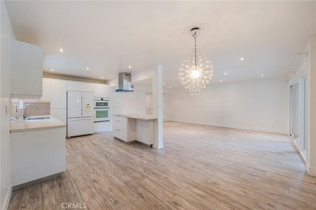 kitchen featuring white appliances, a sink, light countertops, wall chimney exhaust hood, and recessed lighting