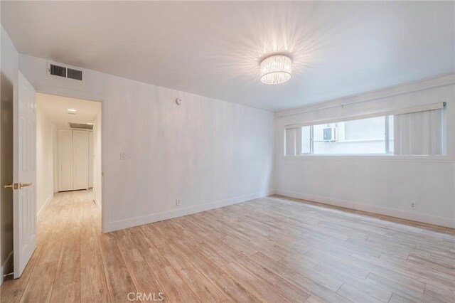 empty room with light wood-type flooring, baseboards, and a chandelier