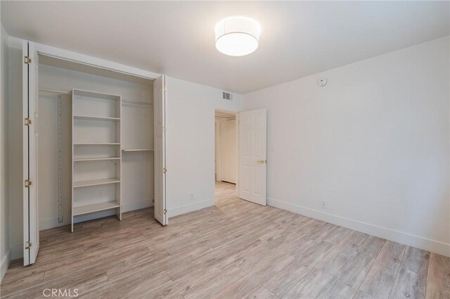 unfurnished bedroom with light wood-style flooring, a closet, and baseboards