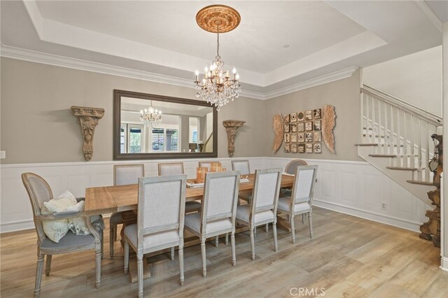dining room featuring a chandelier, a tray ceiling, stairway, a decorative wall, and wood finished floors