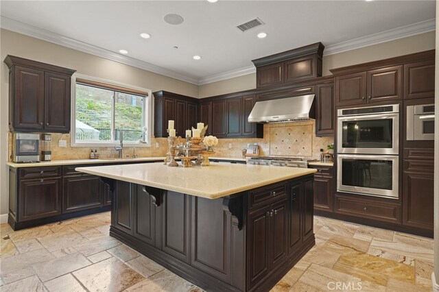 kitchen with stainless steel appliances, stone tile floors, wall chimney range hood, a sink, and light countertops