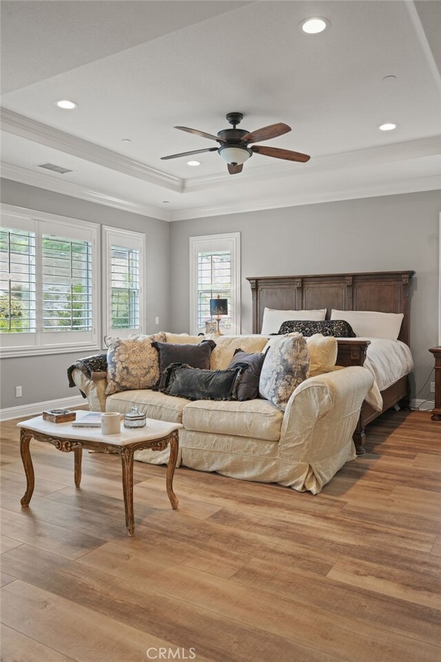 bedroom with light wood-type flooring, a raised ceiling, baseboards, recessed lighting, and ornamental molding