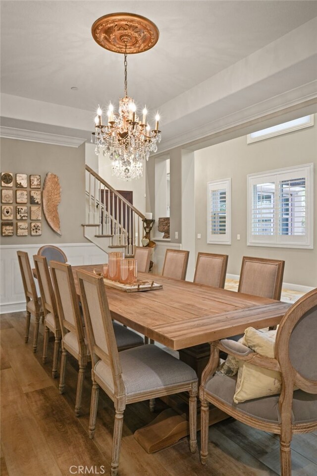 dining area with stairs, a chandelier, wood finished floors, wainscoting, and ornamental molding