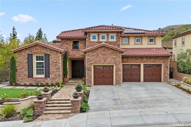 mediterranean / spanish-style home with driveway, a tiled roof, solar panels, an attached garage, and fence
