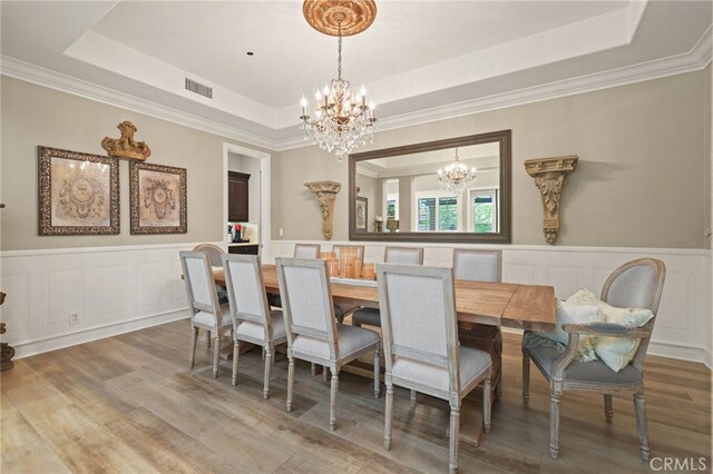dining space with a chandelier, a raised ceiling, wood finished floors, wainscoting, and ornamental molding