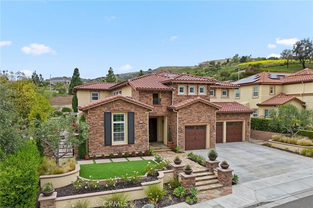 mediterranean / spanish-style home featuring concrete driveway, stone siding, a tile roof, a garage, and stucco siding