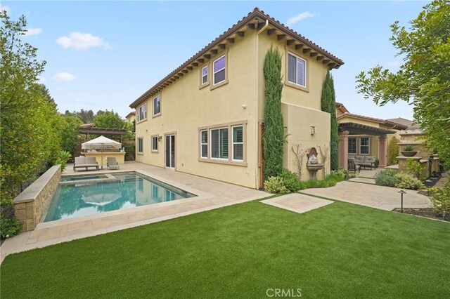 rear view of house with an outdoor kitchen, a lawn, a patio, and stucco siding