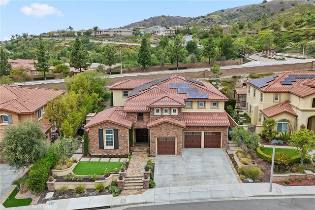 mediterranean / spanish-style home featuring concrete driveway, stone siding, roof mounted solar panels, a tiled roof, and a mountain view