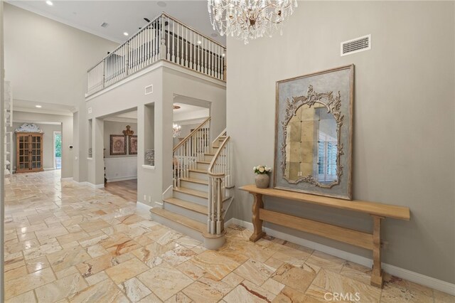 foyer entrance featuring a chandelier, baseboards, a towering ceiling, stone tile floors, and stairs
