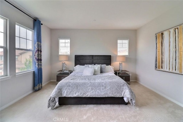 bedroom with multiple windows, light carpet, and baseboards