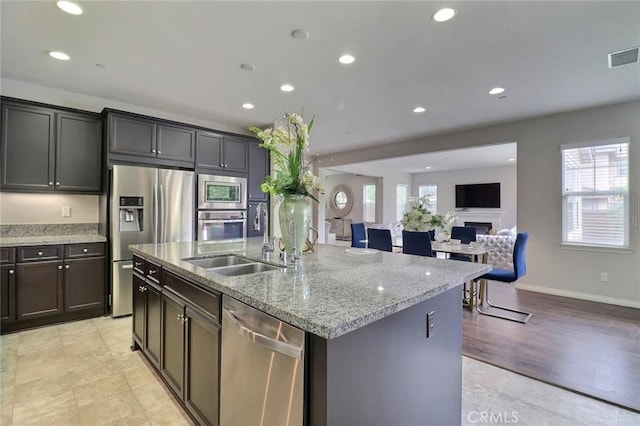 kitchen with appliances with stainless steel finishes, a sink, light stone counters, a center island with sink, and recessed lighting