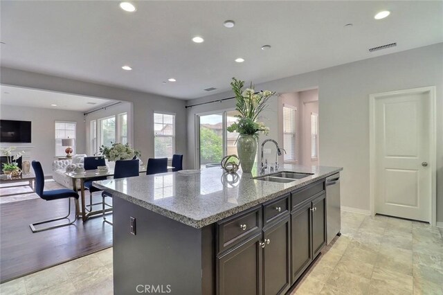 kitchen with a sink, stainless steel dishwasher, light stone countertops, a kitchen island with sink, and recessed lighting