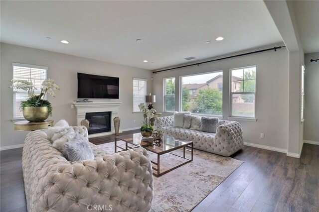 living room featuring baseboards, dark wood-type flooring, a glass covered fireplace, and recessed lighting