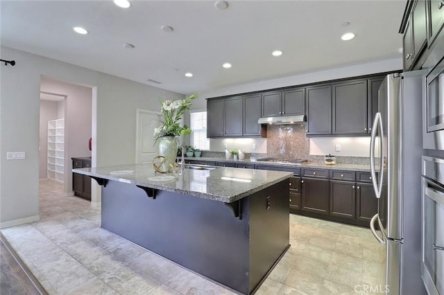 kitchen with stainless steel appliances, a sink, under cabinet range hood, light stone countertops, and recessed lighting