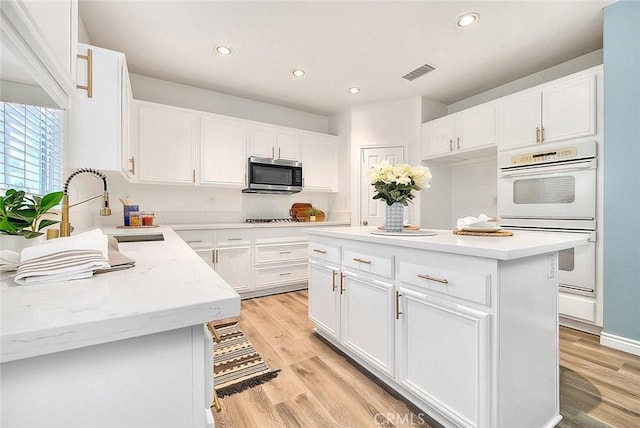 37089 Meadow Brook Way, Beaumont, CA 92223 - kitchen with stainless steel microwave, white double oven, a sink, light wood finished floors, and recessed lighting