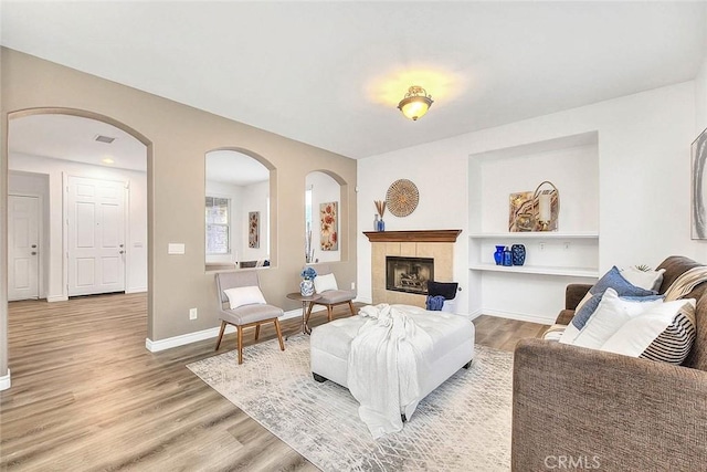 37089 Meadow Brook Way, Beaumont, CA 92223 - living room with light wood-type flooring, baseboards, built in shelves, a tiled fireplace, and arched walkways