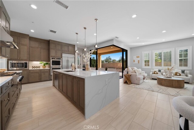 kitchen with built in appliances, a sink, open floor plan, recessed lighting, and under cabinet range hood