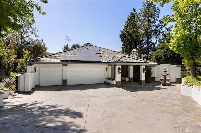 single story home featuring concrete driveway, a garage, roof mounted solar panels, a chimney, and stucco siding