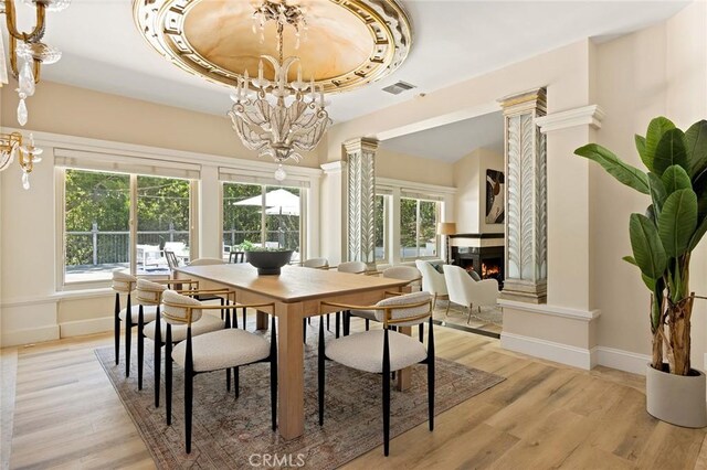 dining space with a chandelier, a multi sided fireplace, light wood-style flooring, and baseboards