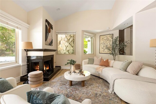 living room with a warm lit fireplace, vaulted ceiling, wood finished floors, and baseboards