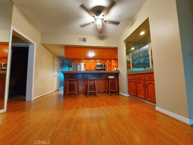 kitchen featuring appliances with stainless steel finishes, ceiling fan, a kitchen breakfast bar, and light wood finished floors