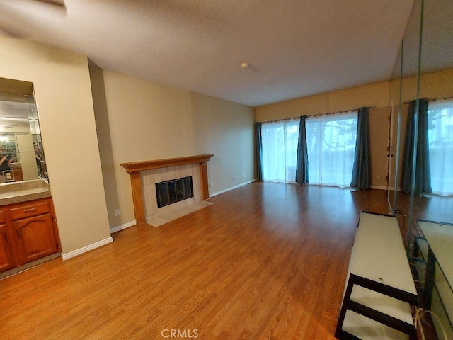 unfurnished living room featuring light wood-type flooring, a tile fireplace, and baseboards