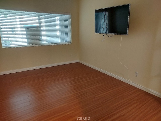 spare room with wood finished floors, plenty of natural light, and baseboards