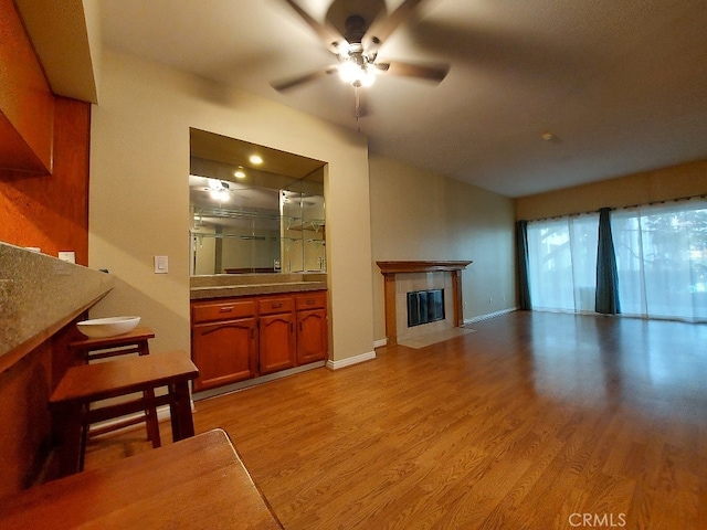 living area with a ceiling fan, light wood-style floors, a tile fireplace, and baseboards