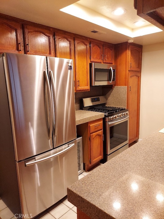 kitchen with stainless steel appliances, brown cabinets, a tray ceiling, light countertops, and recessed lighting