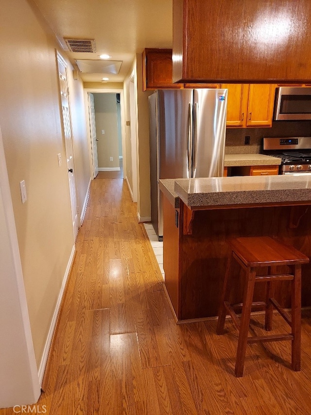 kitchen featuring appliances with stainless steel finishes, light wood finished floors, a kitchen bar, baseboards, and recessed lighting