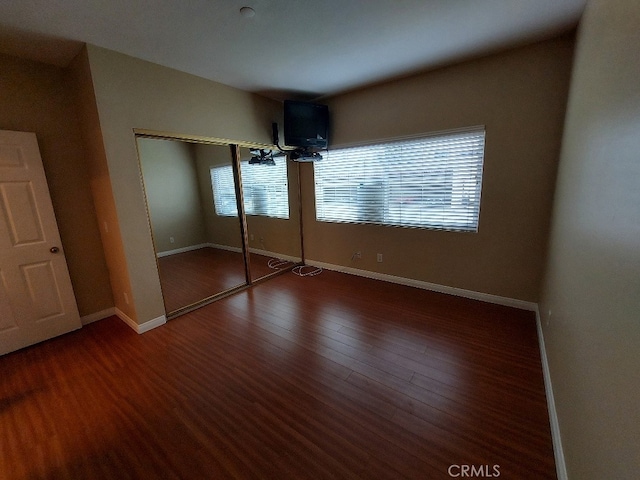 unfurnished bedroom with wood finished floors, baseboards, and a closet