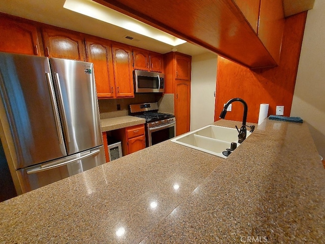 kitchen with appliances with stainless steel finishes, a sink, brown cabinetry, and a peninsula