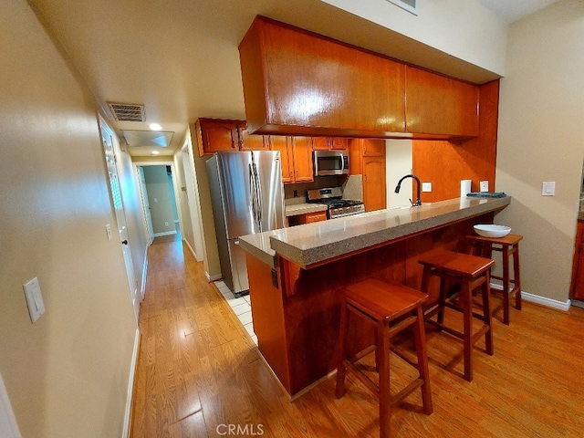 kitchen featuring stainless steel appliances, brown cabinetry, light wood-style floors, a peninsula, and a sink
