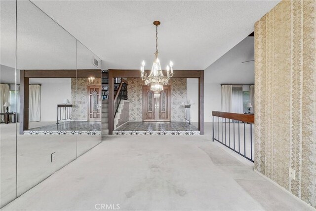 unfurnished dining area with a chandelier, stairs, a textured ceiling, and wallpapered walls