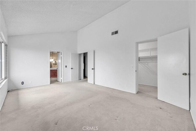 unfurnished bedroom featuring carpet floors, a spacious closet, a textured ceiling, high vaulted ceiling, and ensuite bath