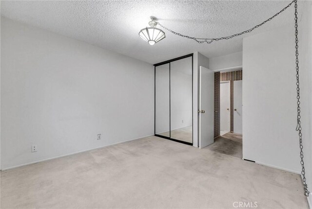 unfurnished bedroom with light carpet, a textured ceiling, and a closet