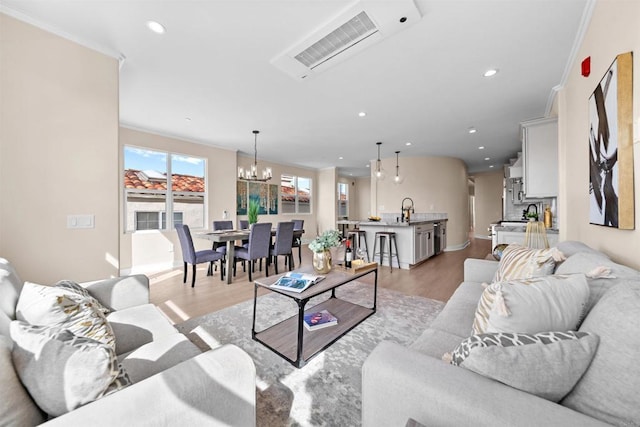 living room featuring a chandelier, light wood-style flooring, crown molding, recessed lighting, and baseboards