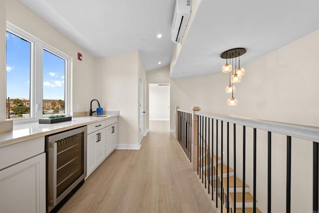 kitchen with wine cooler, light wood-style floors, white cabinetry, a wall unit AC, and a sink