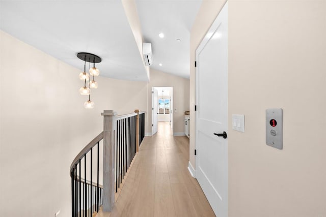 hallway with an upstairs landing, vaulted ceiling, light wood finished floors, a wall mounted air conditioner, and baseboards
