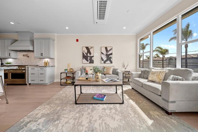 living room with light wood-style floors, crown molding, and recessed lighting