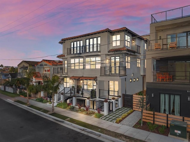 multi unit property with stucco siding, a balcony, and a tiled roof