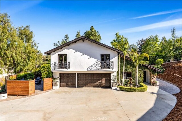 view of home's exterior featuring a balcony, an attached garage, concrete driveway, and stucco siding