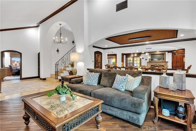 living room featuring arched walkways, crown molding, stairway, a towering ceiling, and wood finished floors