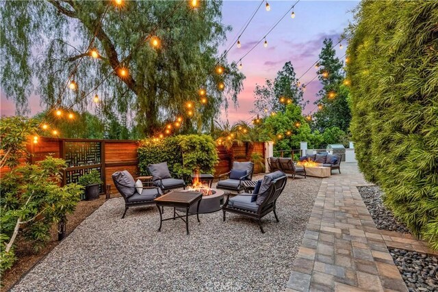 patio terrace at dusk featuring an outdoor living space with a fire pit, a fenced backyard, and area for grilling
